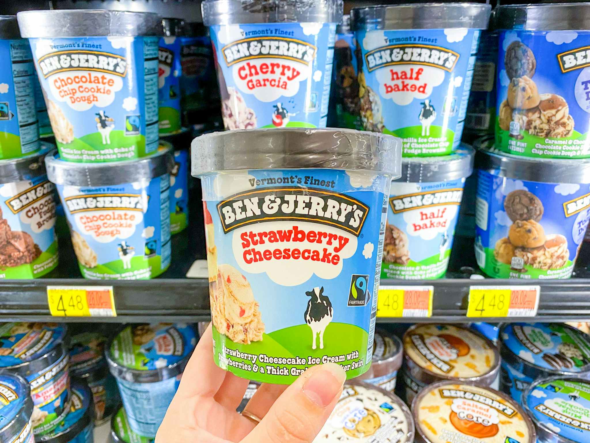 Ben & Jerry's Strawberry Cheesecake Ice Cream held in front of shelf full of Ben & Jerry's products at Walmart