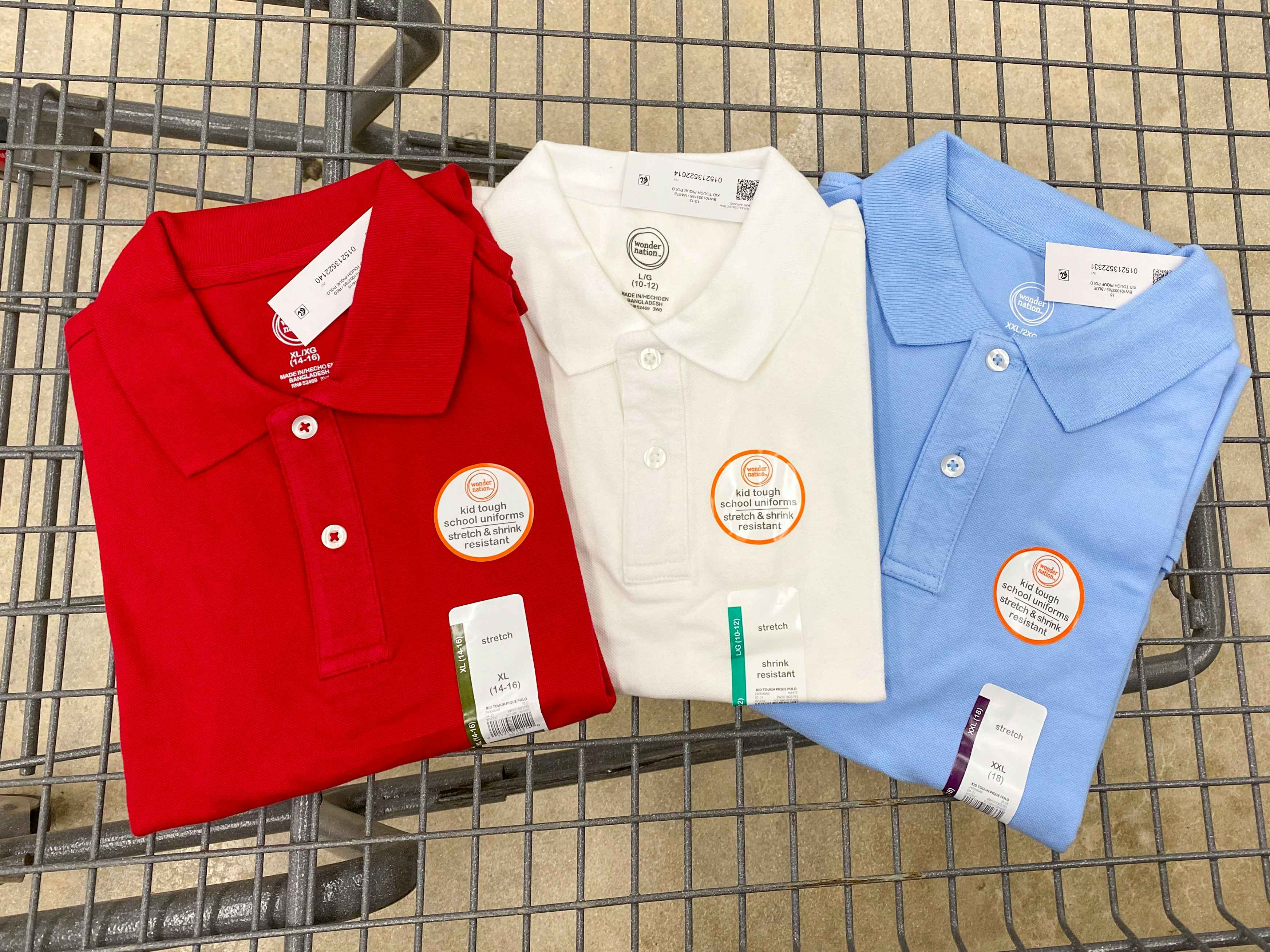 Three different colored children's school uniform shirts in a Walmart shopping cart.