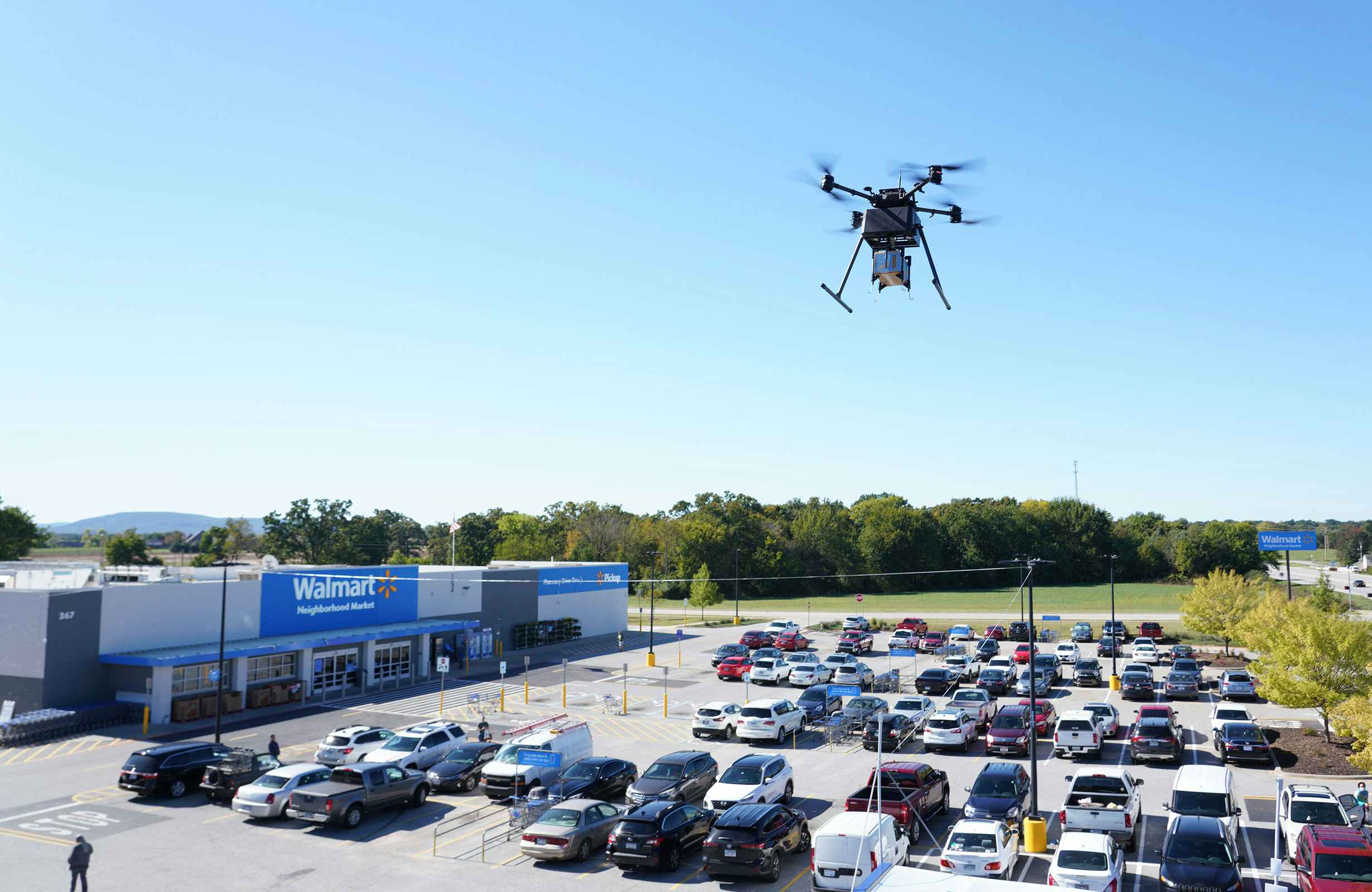 A drone carrying a Walmart delivery box in the sky above a Walmart.