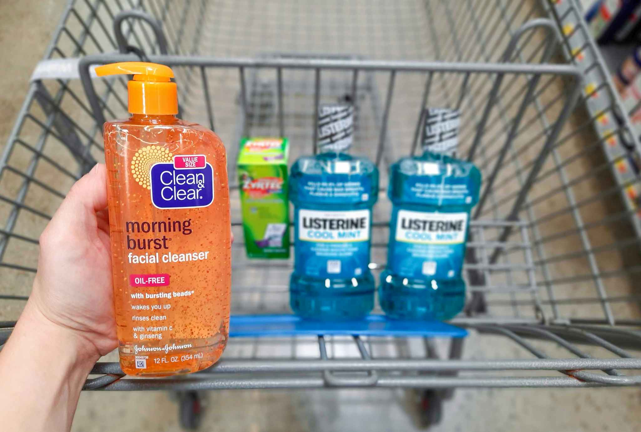 Clean and Clear product held over Walmart shopping cart filled with Zyrtec and Listerine products.