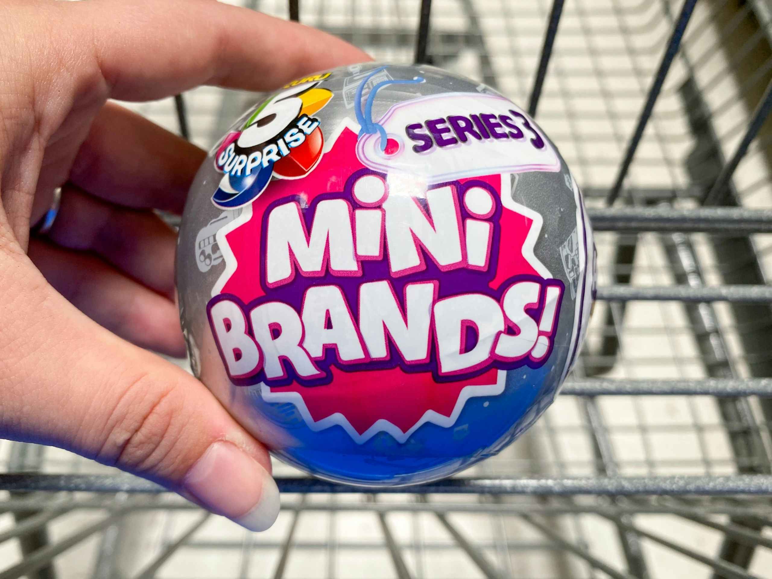Zuru 5 Surprise Mini Brands Mystery Capsule held over Walmart shopping cart