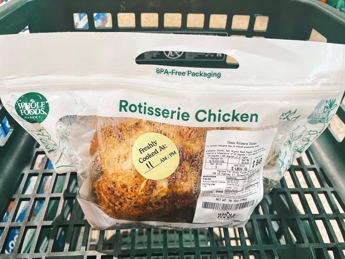 A packaged rotisserie chicken sitting in a shopping cart at Whole Foods.