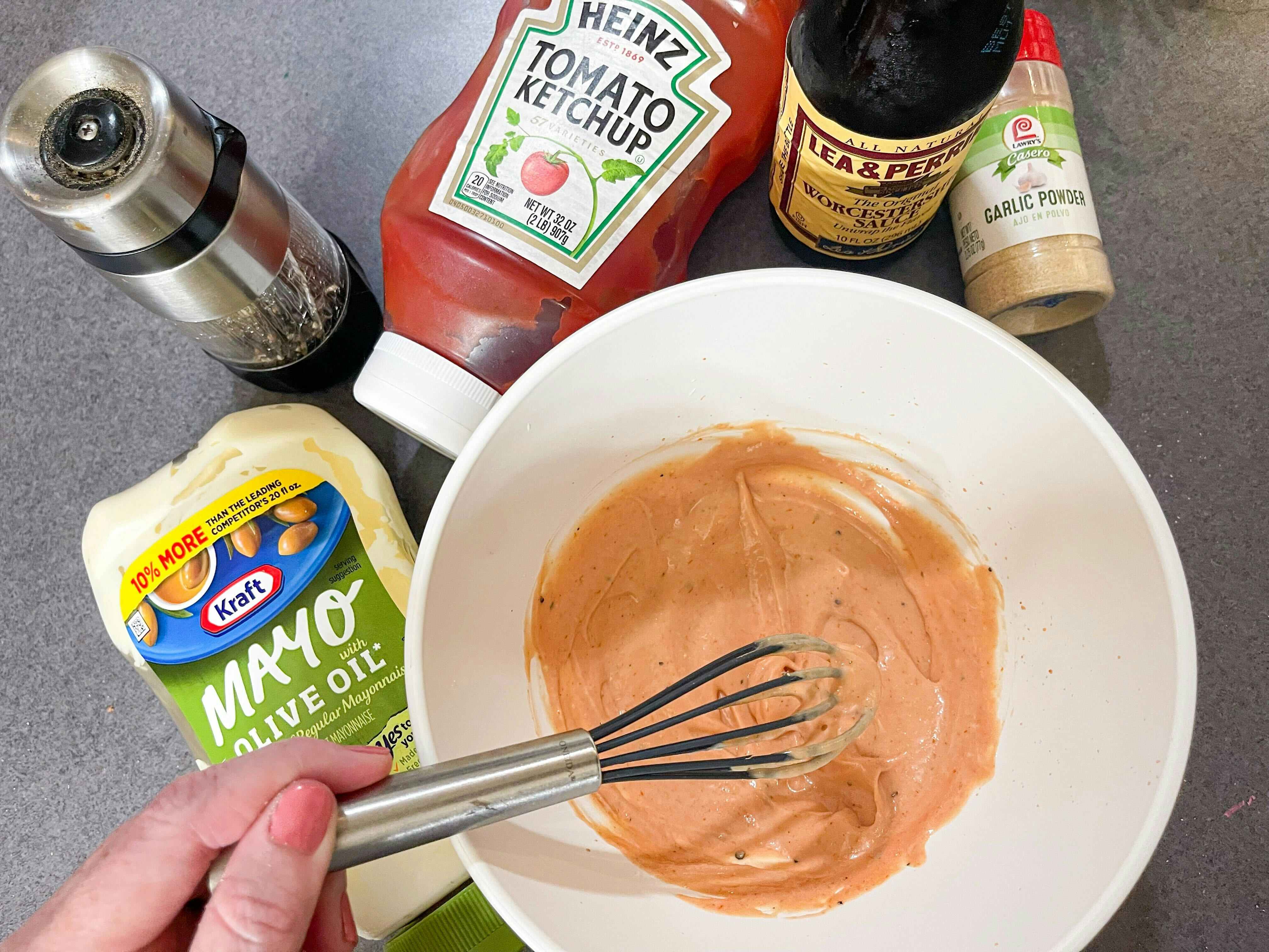 A mixing bowl with homemade sauce with mayo, black pepper, ketchup, Worcestershire sauce, and garlic powder, with a person whisking it 