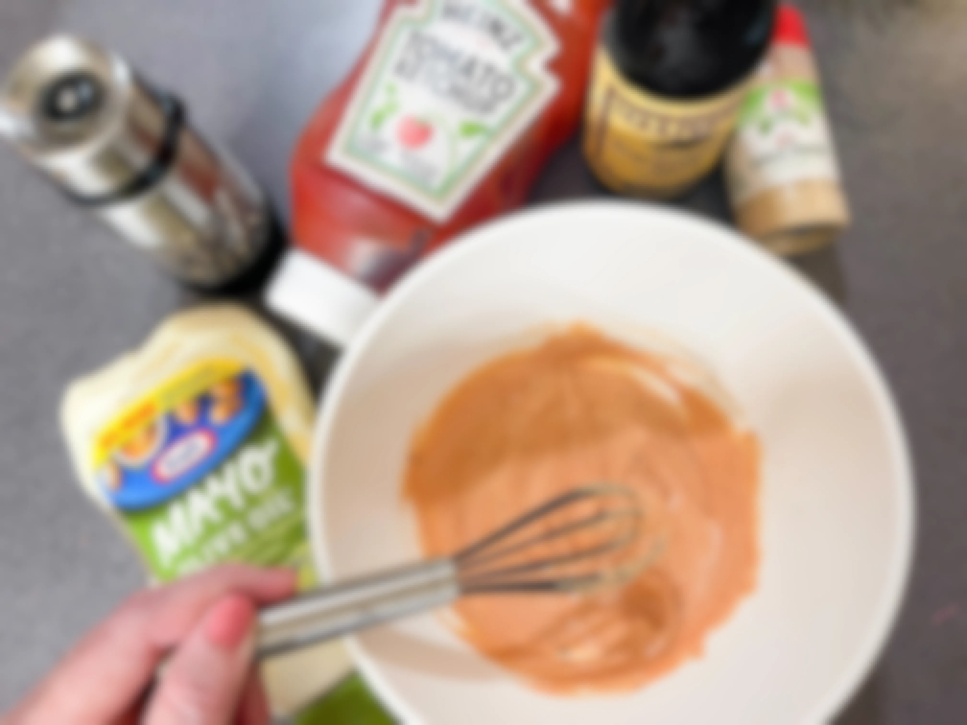 A mixing bowl with homemade sauce with mayo, black pepper, ketchup, Worcestershire sauce, and garlic powder, with a person whisking it 