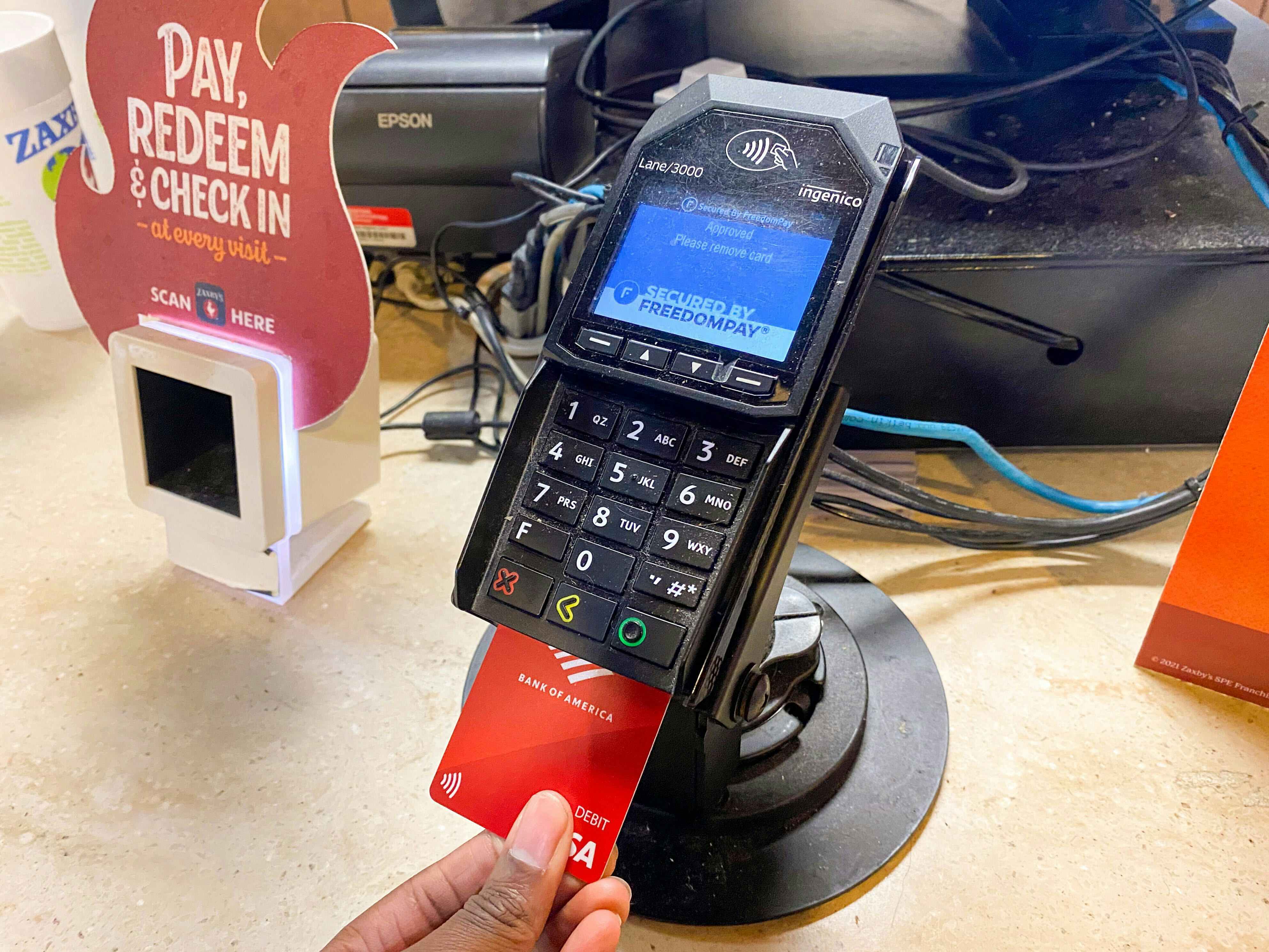 A person's hand inserting their credit card into the card reader at the counter of Zaxby's.