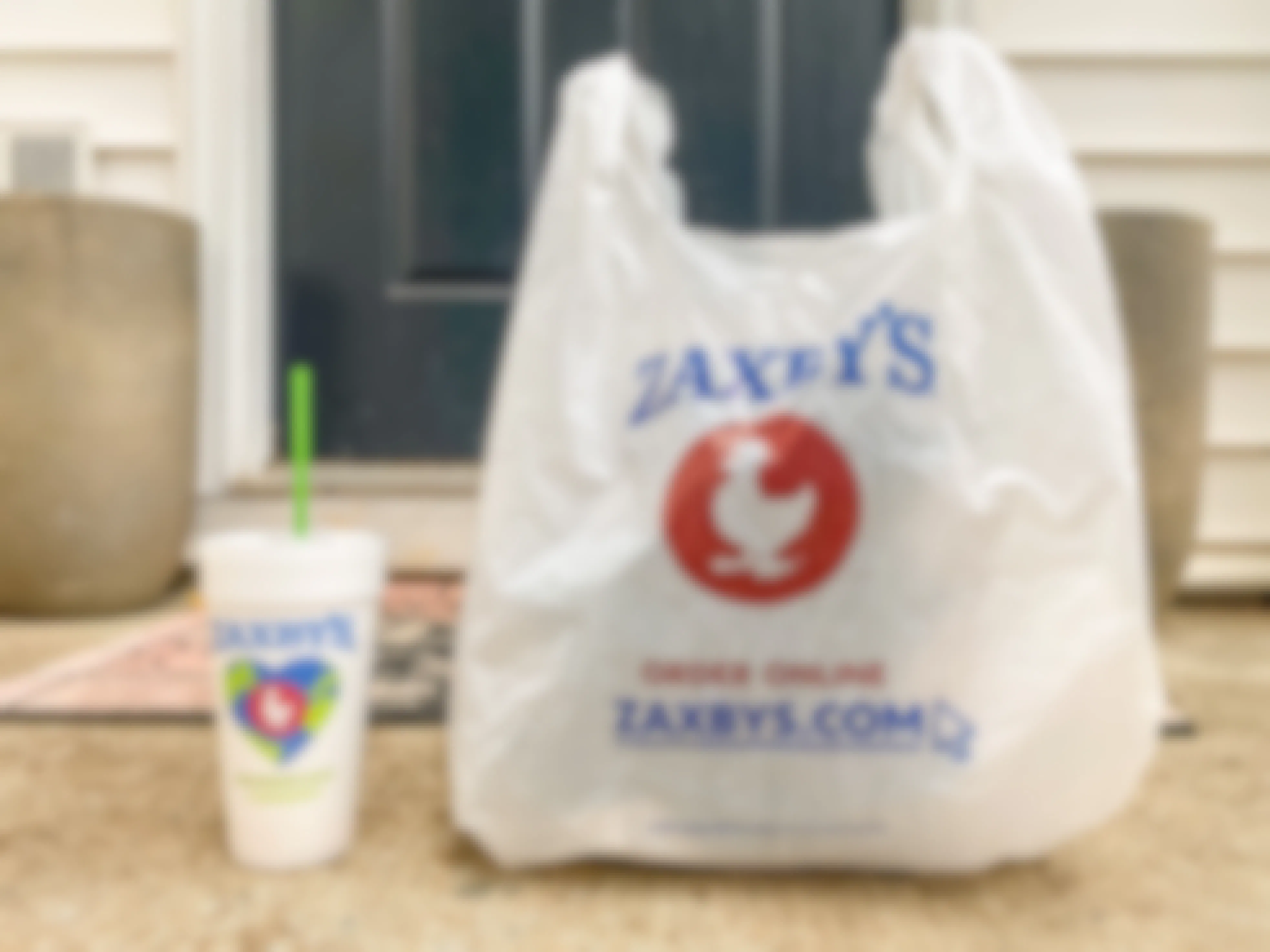 A Zaxby's takeout bag and drink sitting on a front porch.