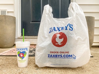 A Zaxby's takeout bag and drink sitting on a front porch.