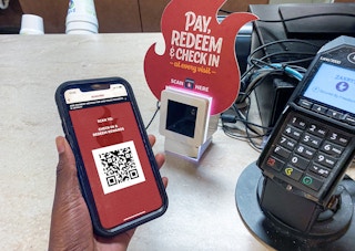 A person's hand holding a cell phone displaying the Zaxby's app's QR code for checking in at the restaurant.