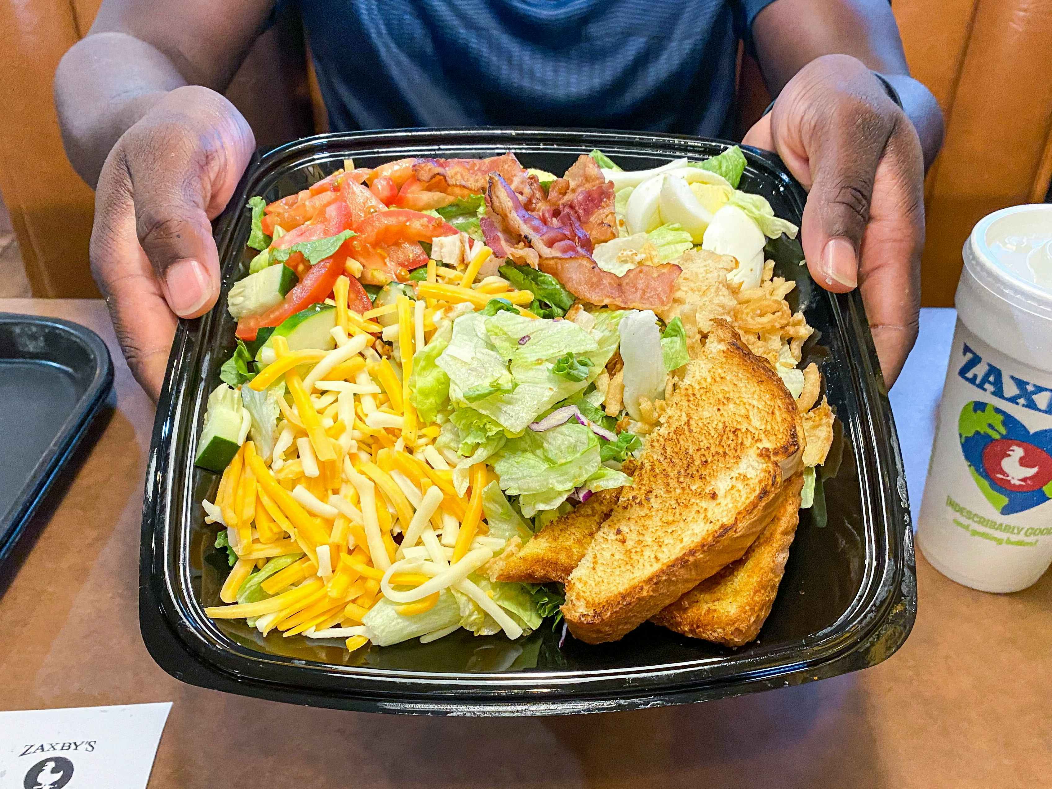 A person holding up a Zaxby's salad while sitting in a booth at Zaxby's.