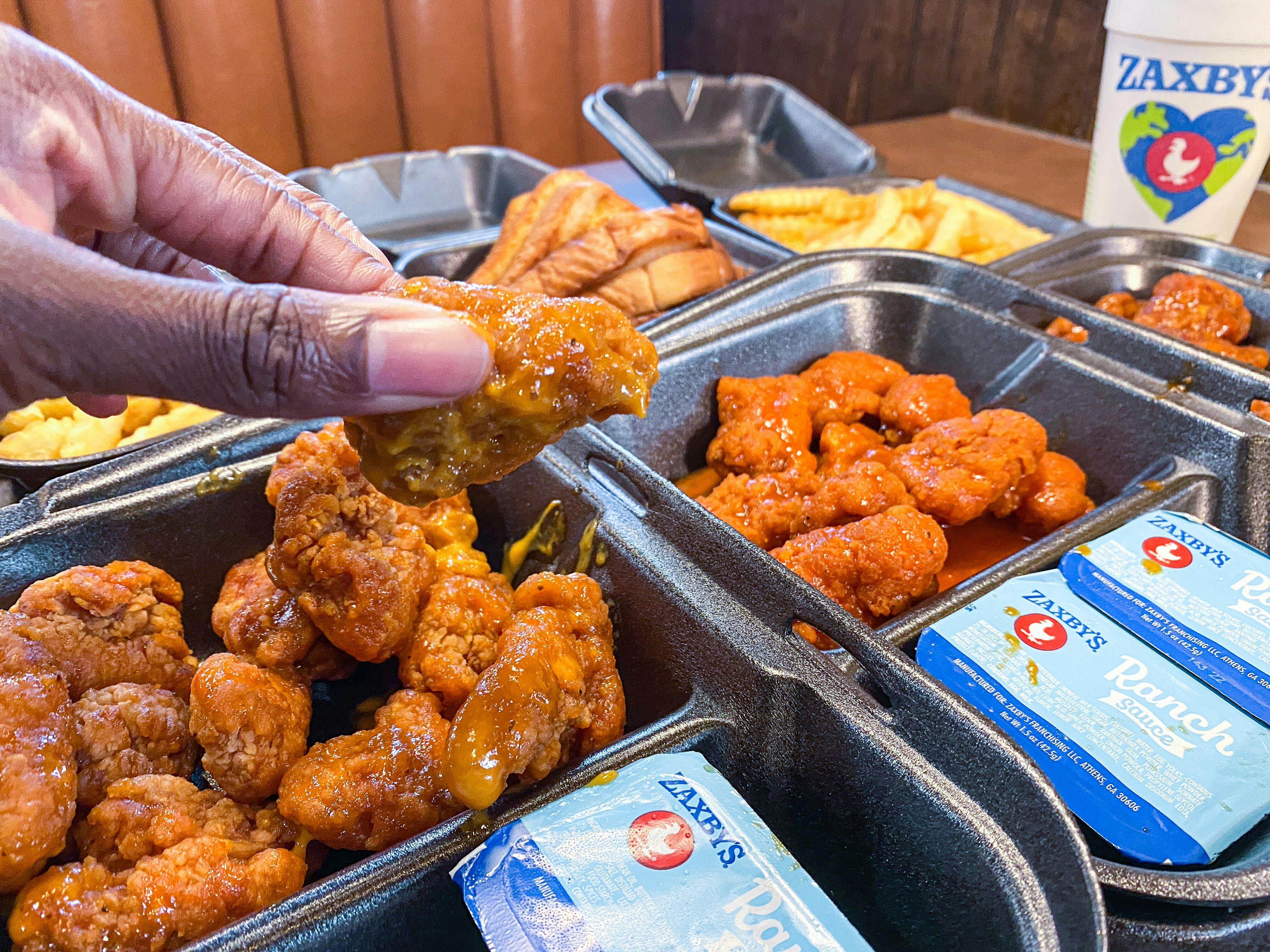 A person's hand taking a piece of chicken out of a box of boneless chicken wings on a table at Zaxby's.