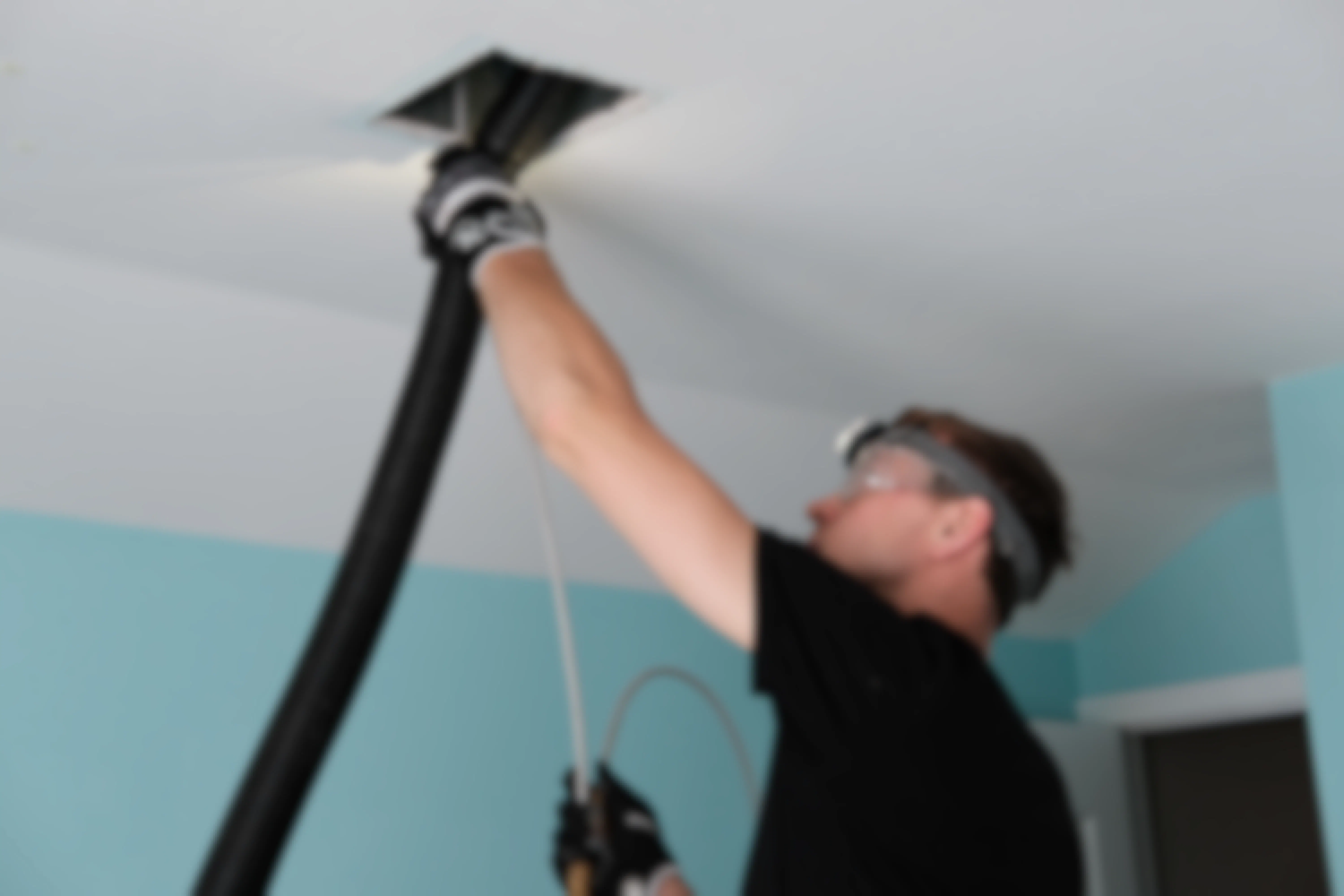 A man using a vaccum hose to clean out an air duct through a vent hole.