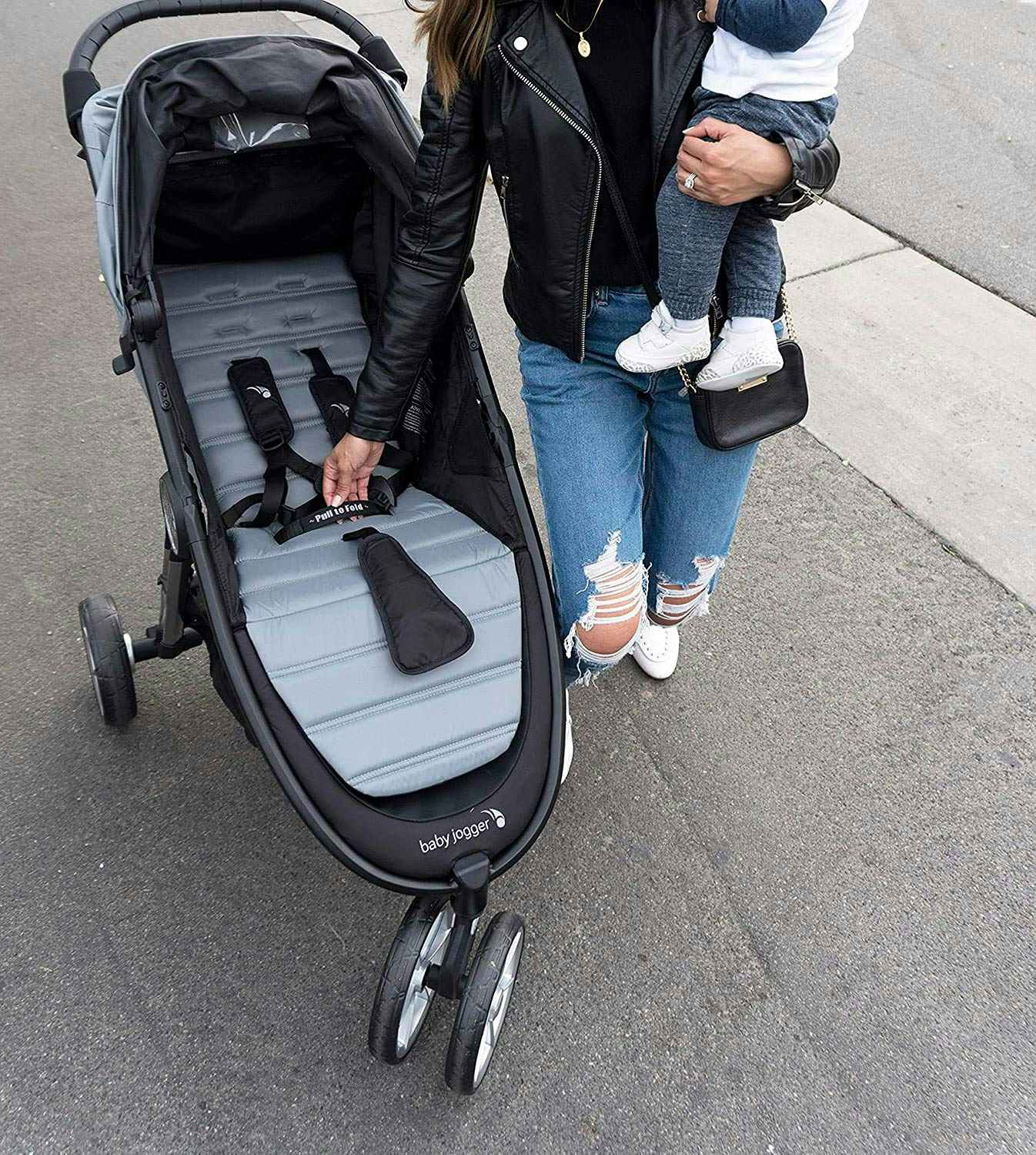 A woman preparing a Baby Jogger stroller while she holds her child.