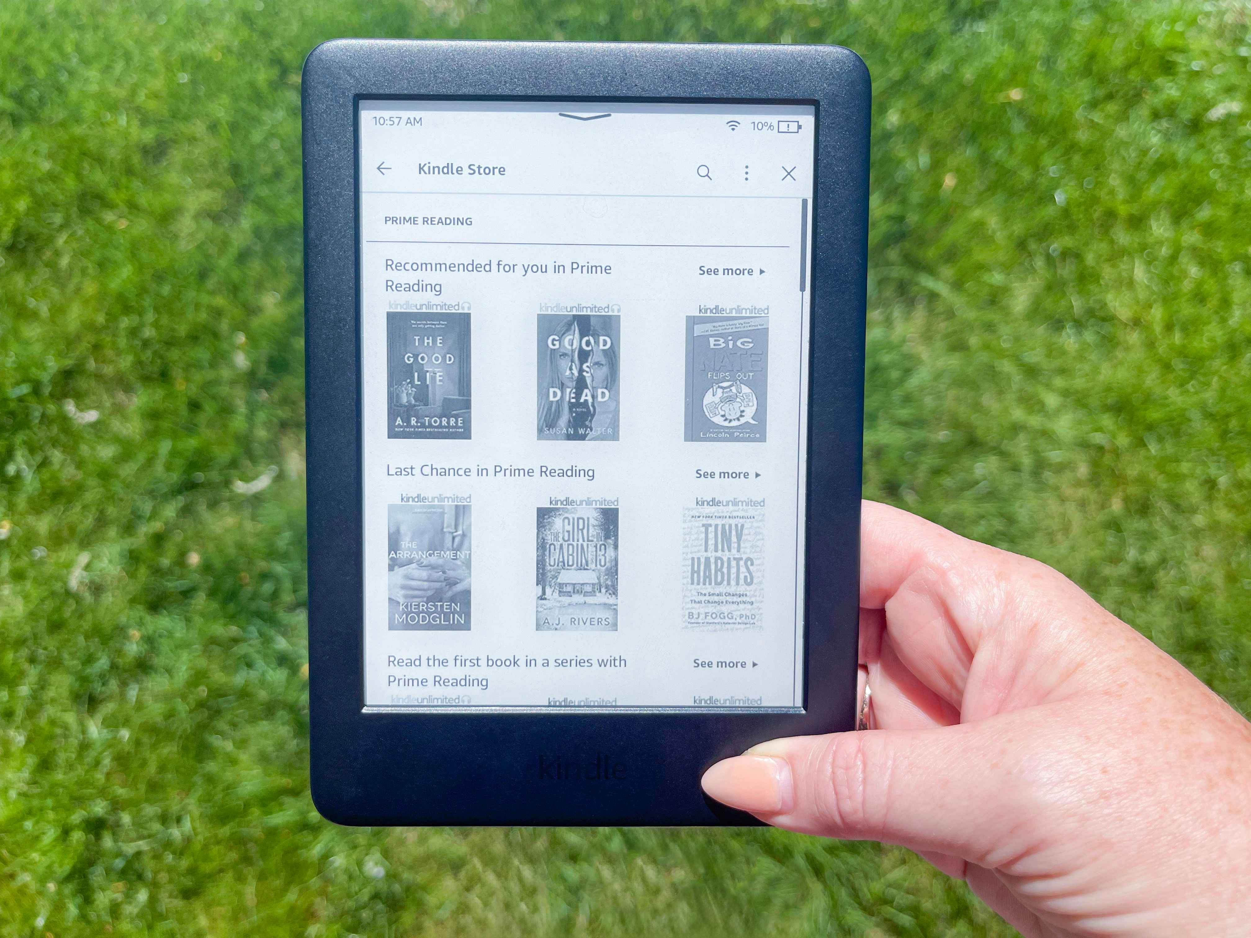 A person holding an Amazon Kindle while standing on some grass outside.