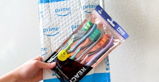 person holding reach essentials toothbrushes and caps along with amazon package