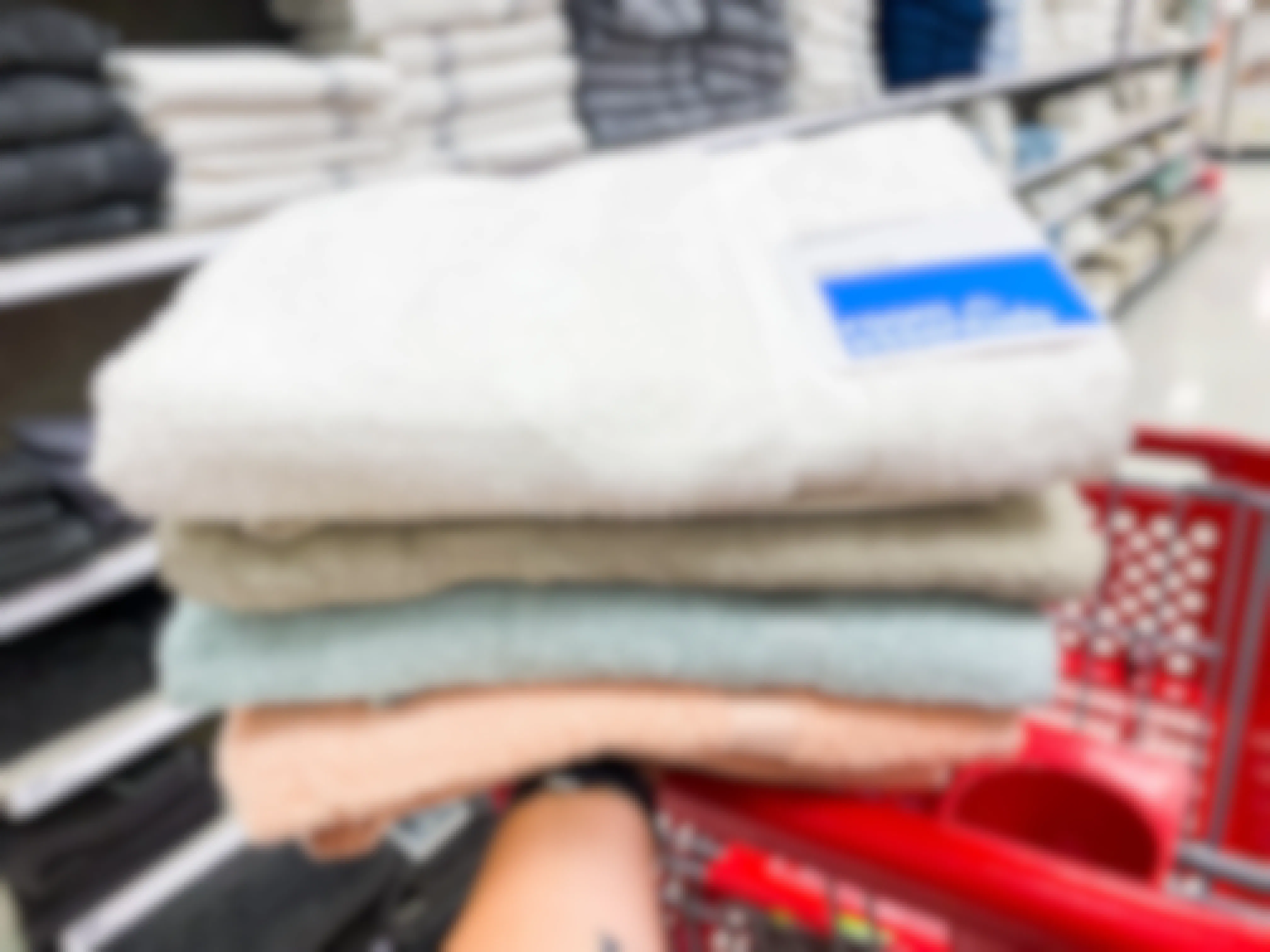 A person holding four Room Essentials bath towels next to a target shopping cart