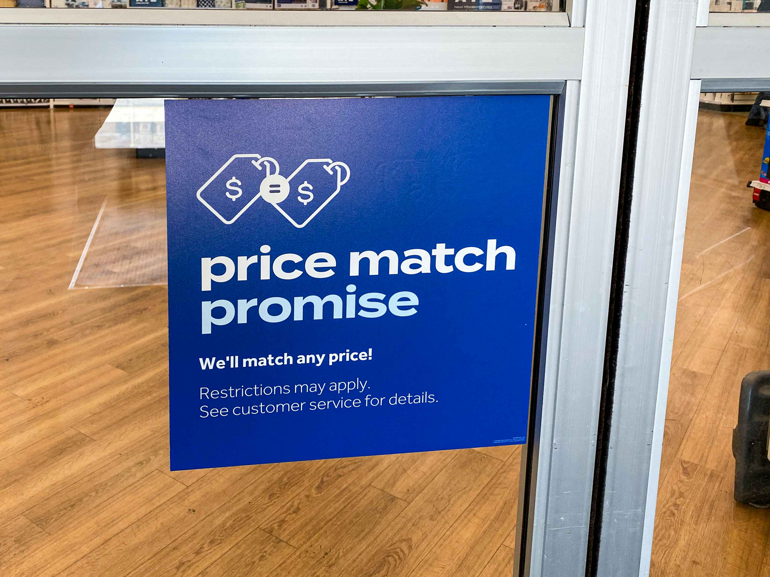 A sign on the window of the Bed Bath & Beyond entrance which reads, "Price match promise. We'll match any price! Restrictions may apply. See customer service for details.