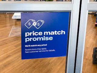 A sign on the window of the Bed Bath & Beyond entrance which reads, "Price match promise. We'll match any price! Restrictions may apply. See customer service for details.