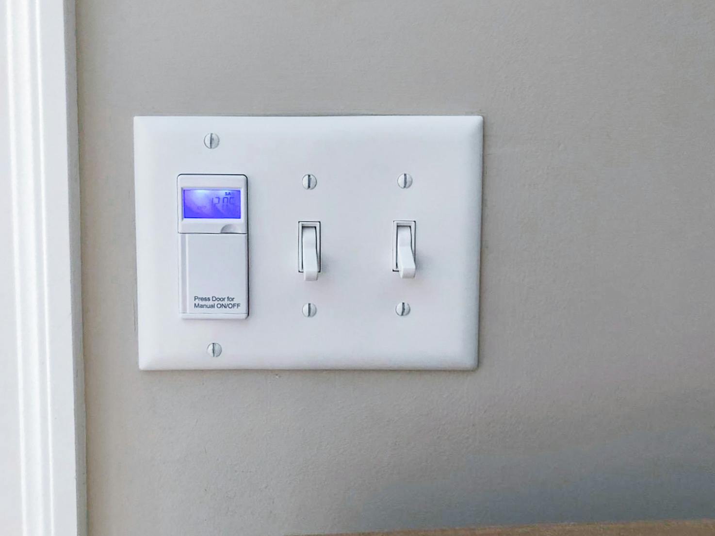 A programmable light switch timer installed next to two normal light switches on a wall.