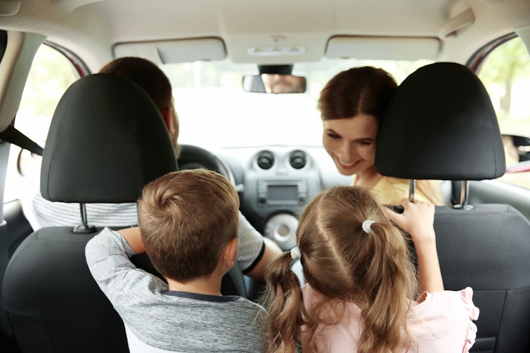 Two adults in the front seats of a car with two children in the backseat.
