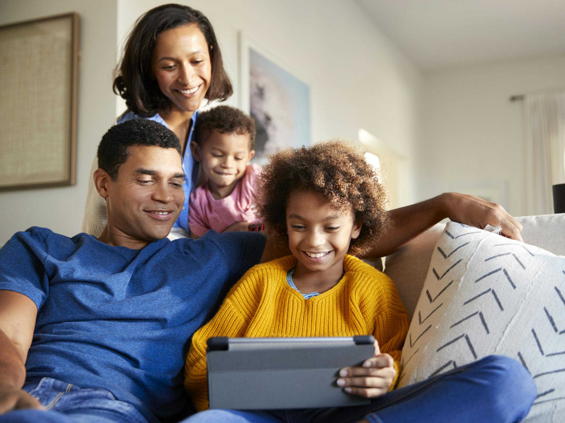 happy family sitting together in living room looking down at tablet