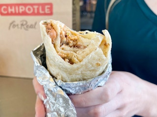 A person holding a burrito that has bitten into. The beans chicken and rice are visible inside.