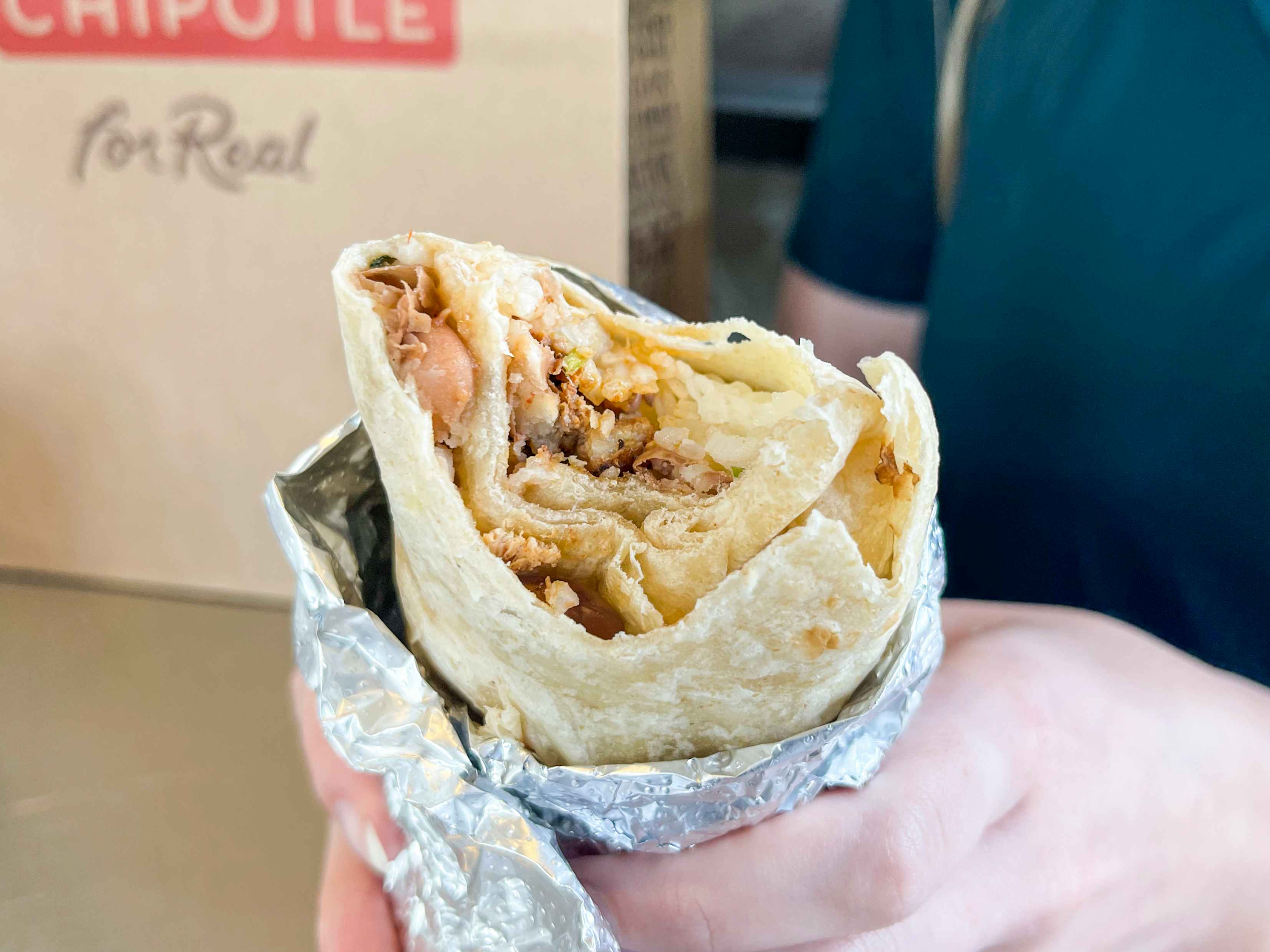 A person holding a chipotle secret menu burrito that has bitten into. The beans chicken and rice are visible inside.