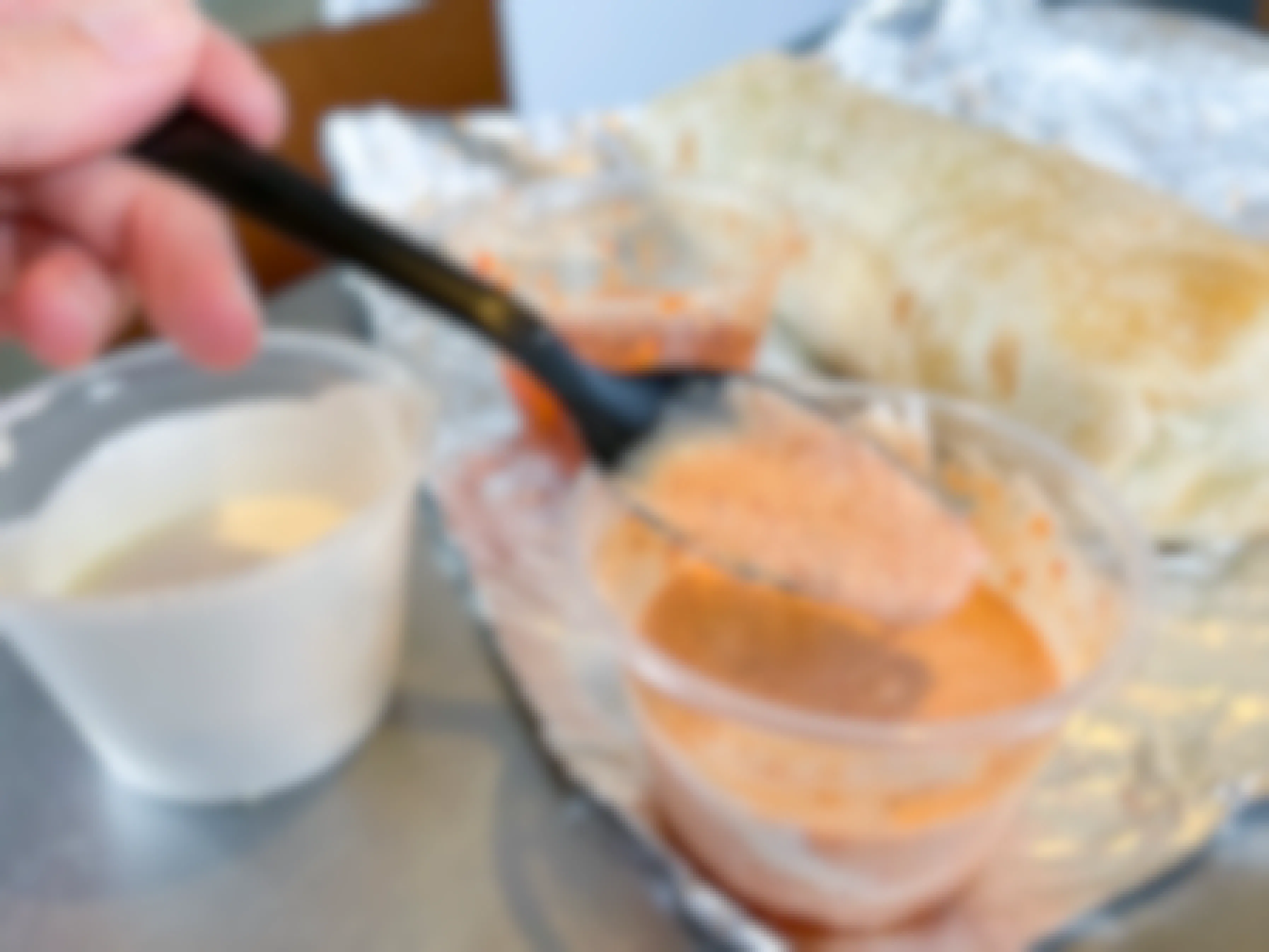 A black plastic spoon in a container filled with a pinkish colored sauce. Beside it are two sauce containers with sour cream and a hot sauce. Part of the chipotle secret menu.