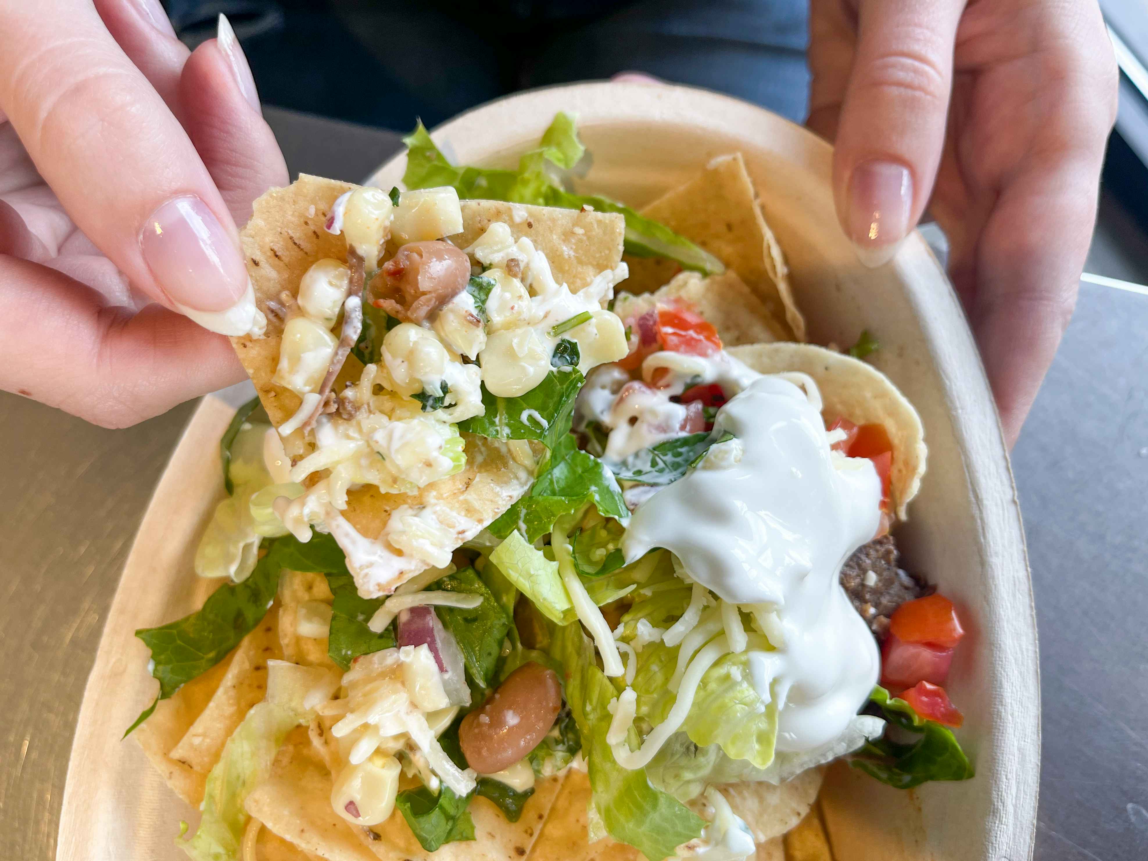 A person scooping up a chip with toppings in a bowl of nachos. Part of the chipotle secret menu.