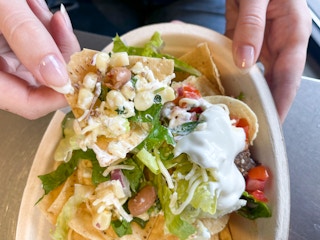 A person scooping up a chip with toppings in a bowl of nachos. Part of the chipotle secret menu.