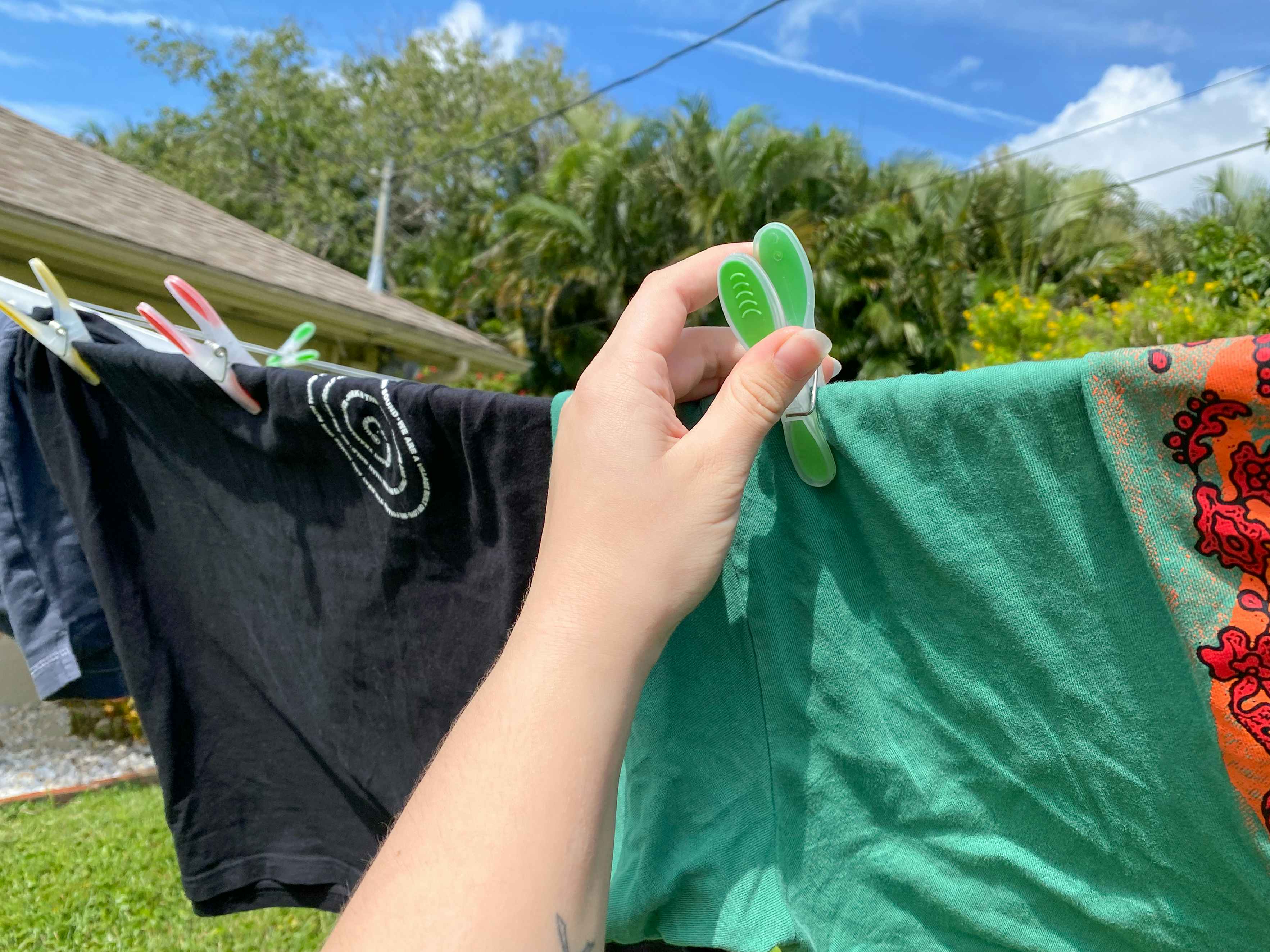 A person's hand using a colorful clothespin to hang a shirt outside to dry on a clothesline.