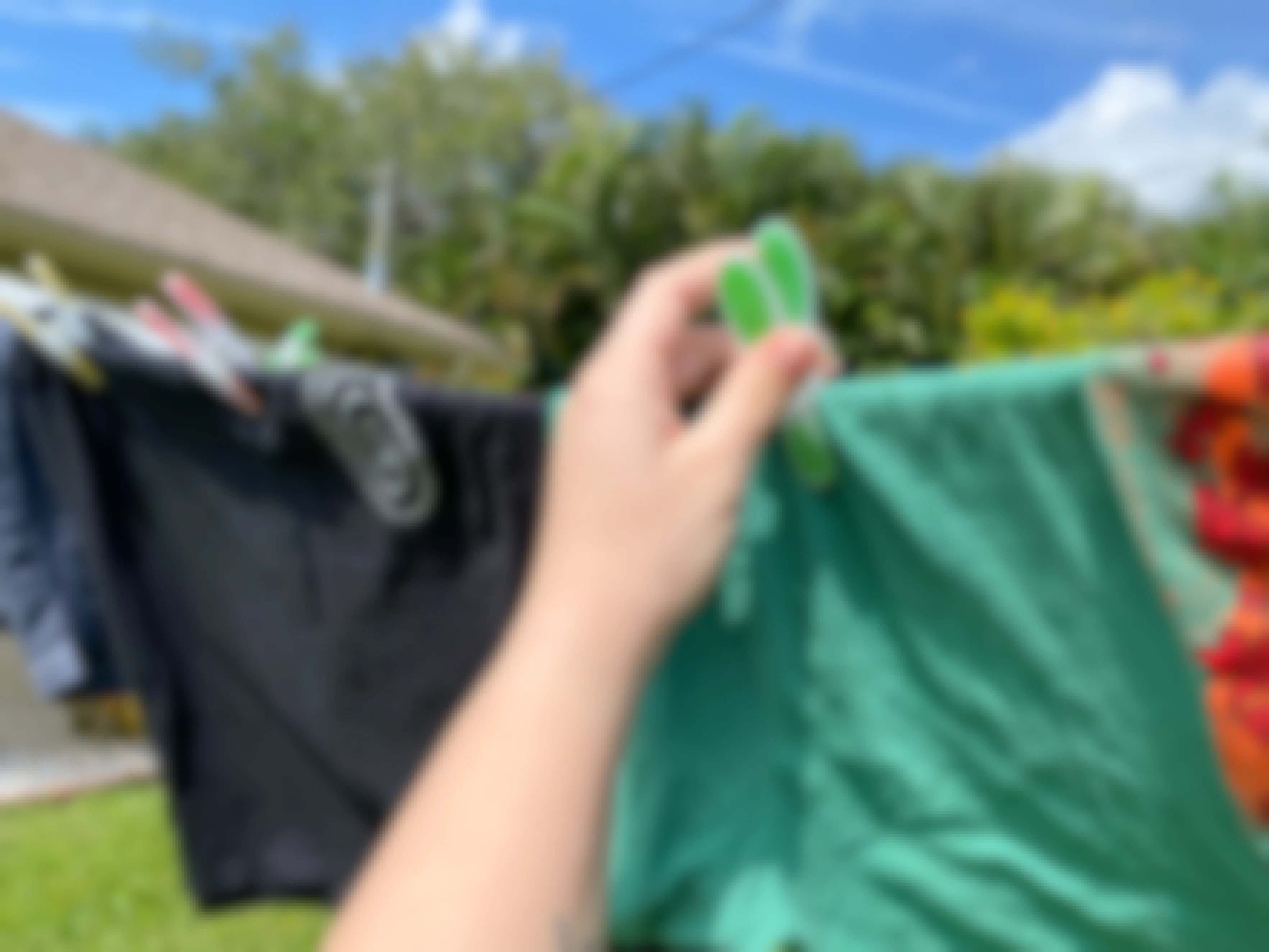 A person's hand using a colorful clothespin to hang a shirt outside to dry on a clothesline.