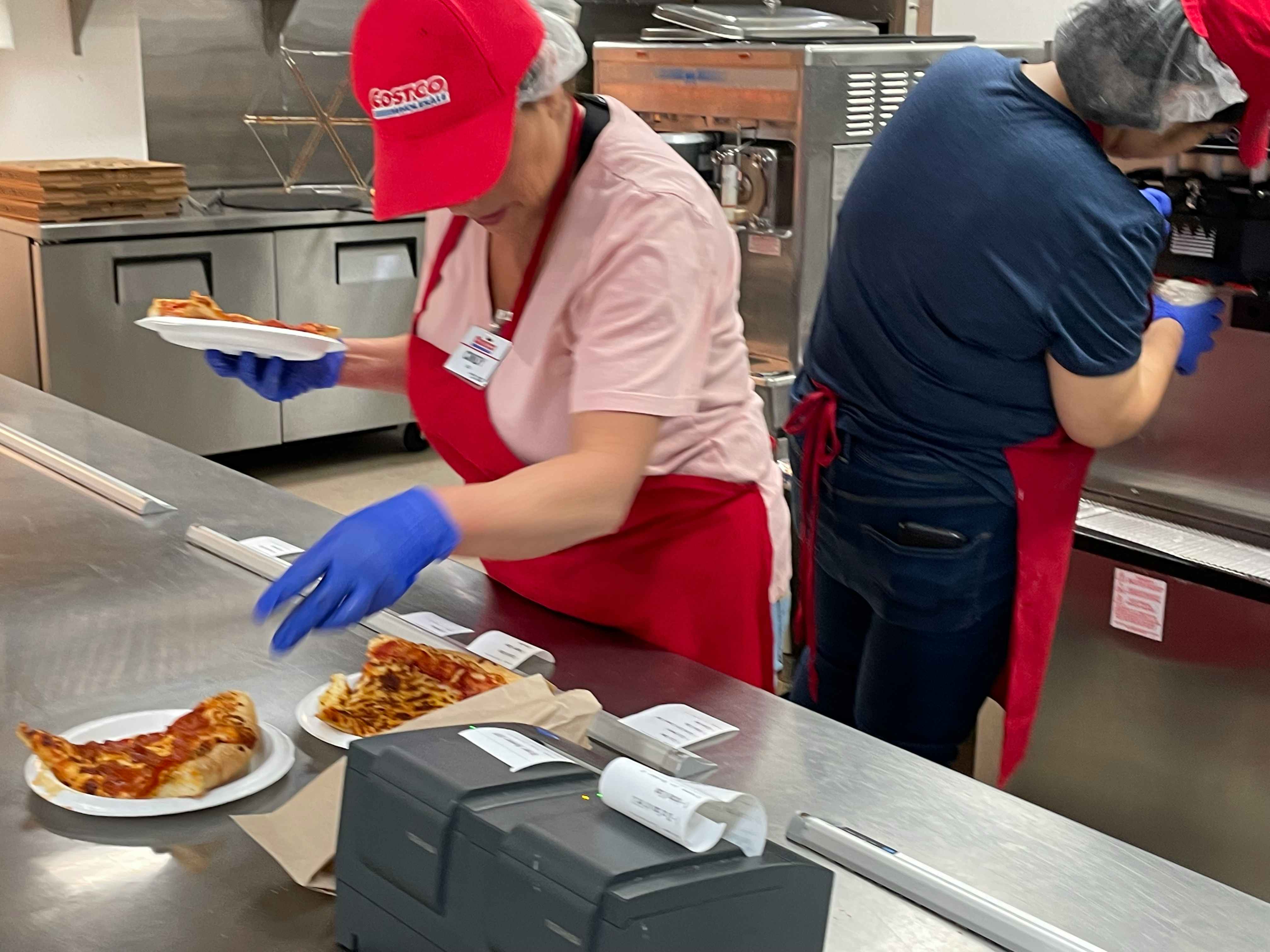 Costco employees preparing an order of pizza slices at the Costco food court