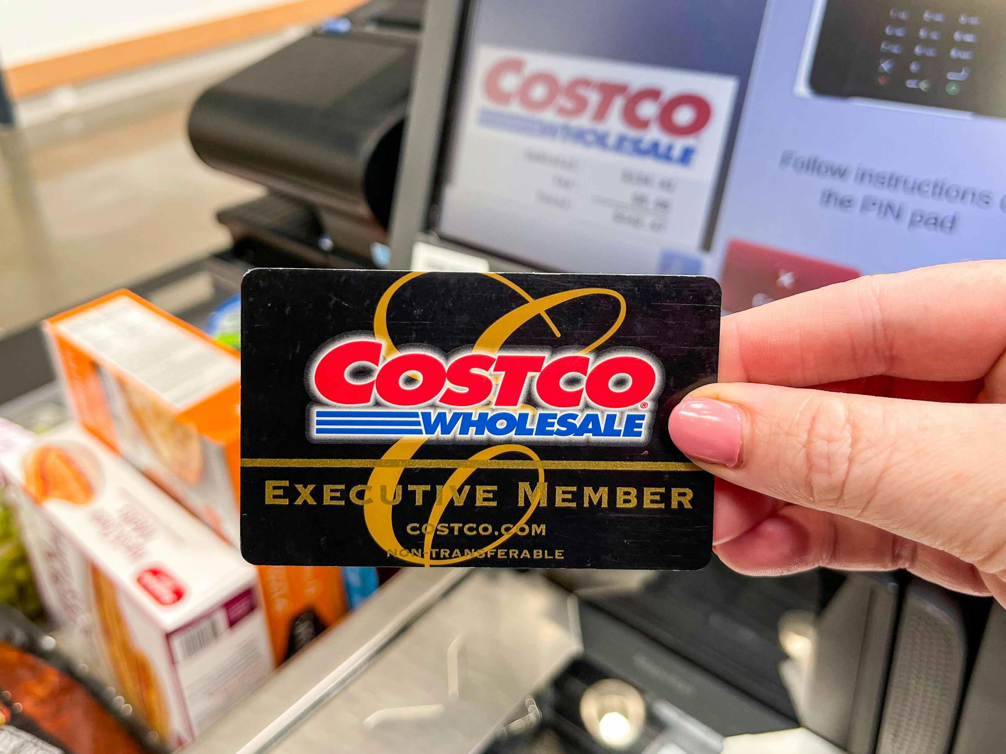 A person's hand holding up their Costco membership card in front of the self-checkout scanner at Costco.