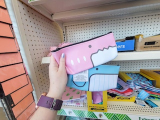 hand holding a pink and a blue animal face pencil pouch
