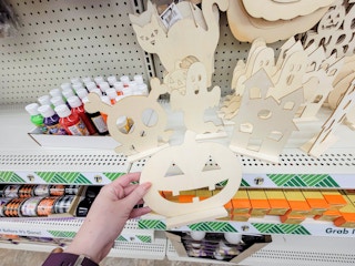 hand holding a wooden pumpkin to paint, by a skull, ghost, and house
