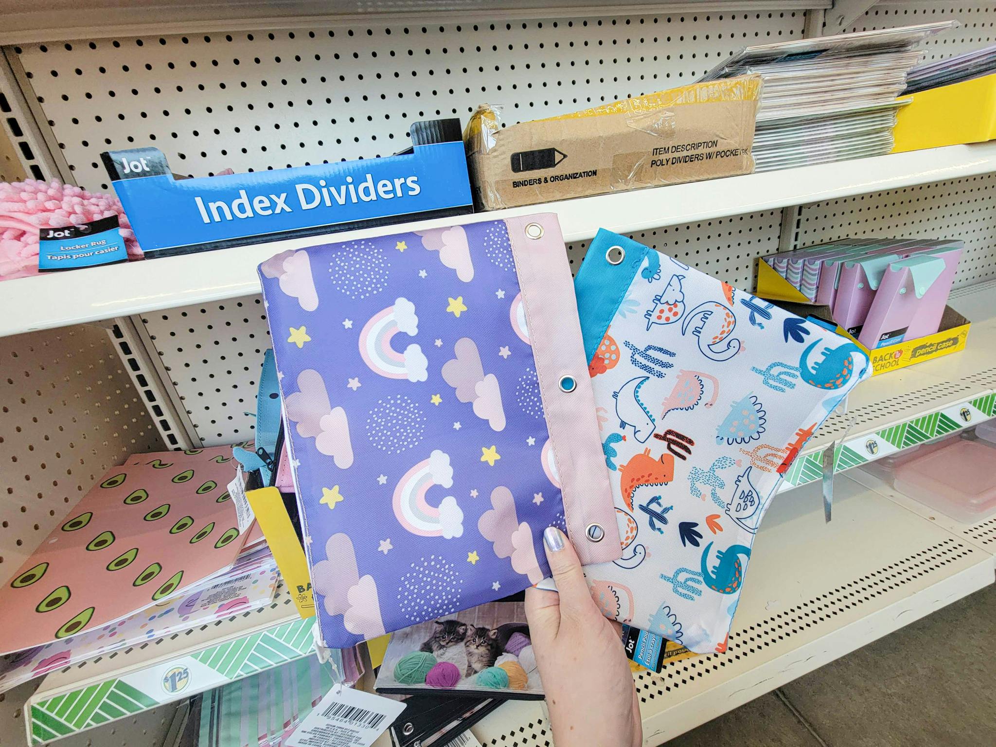hand holding a purple with rainbows pencil binder pouch and a white with dinosaurs pencil binder pouch