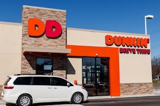 A white mini van pulling up to a Dunkin drive thru.