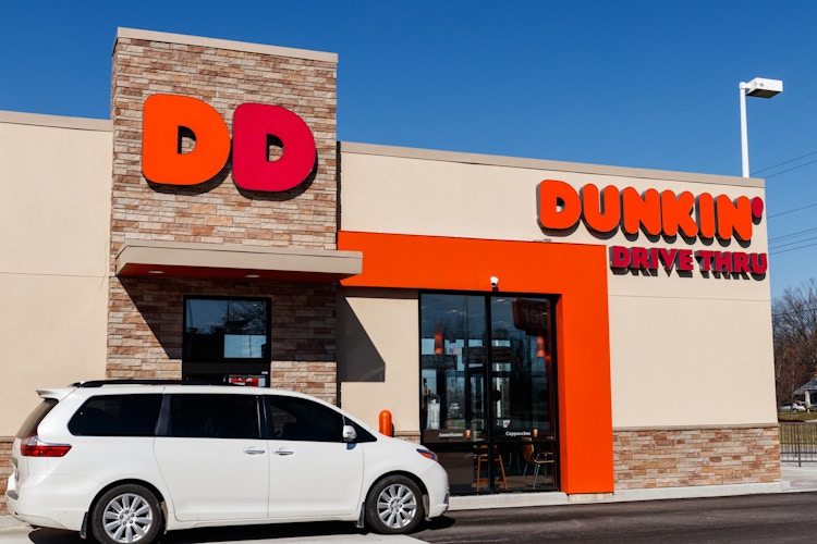 A white mini van pulling up to a Dunkin drive thru.