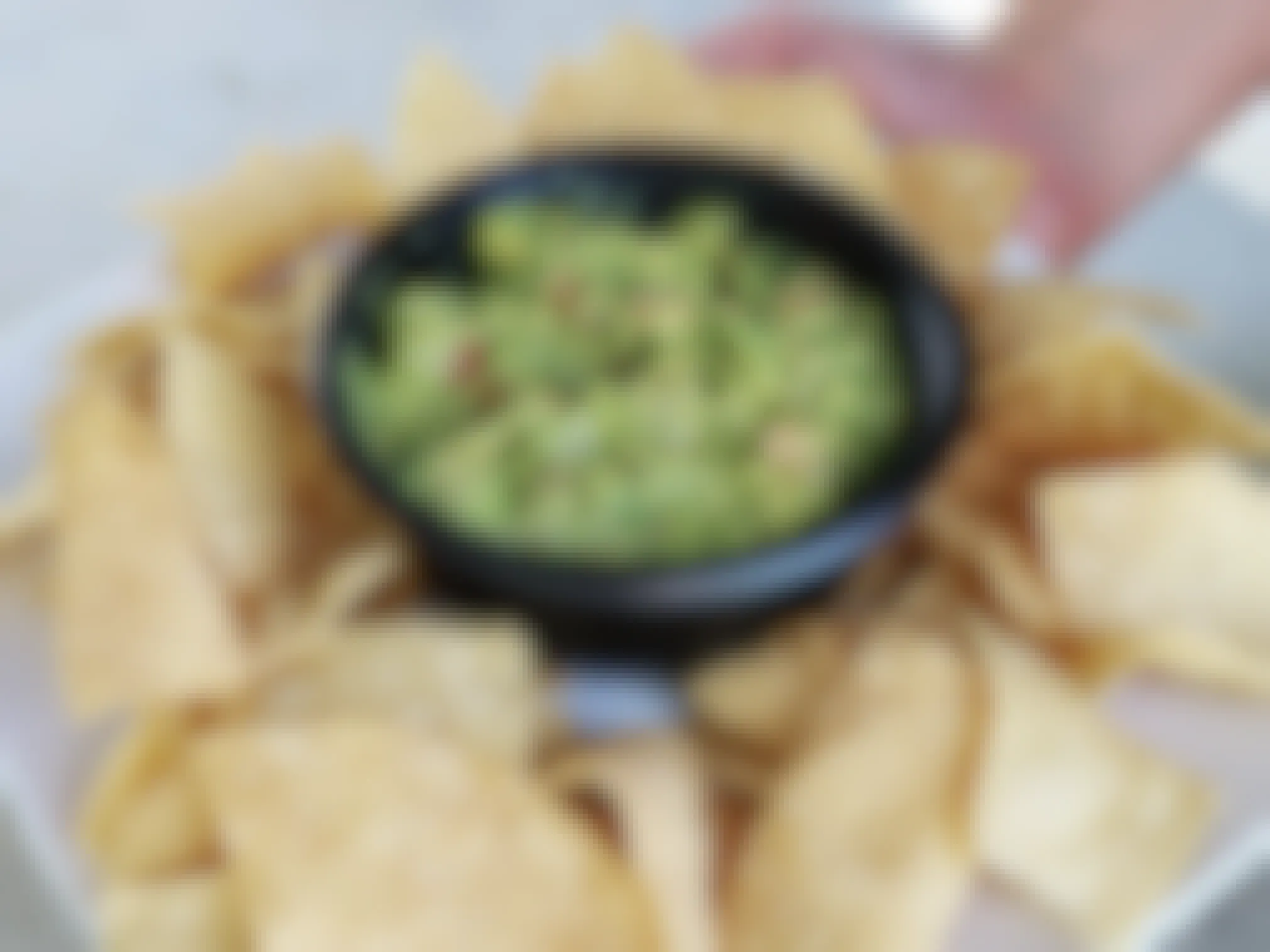 A person's hand putting down a plate of chips with a small bowl of guacamole in the center of the chips.