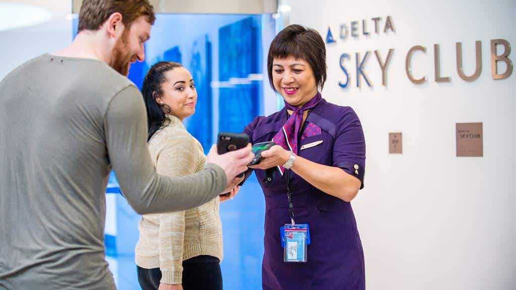 Two Delta passengers being scanned in by a Delta employee in front of a Delta Sky Club sign.