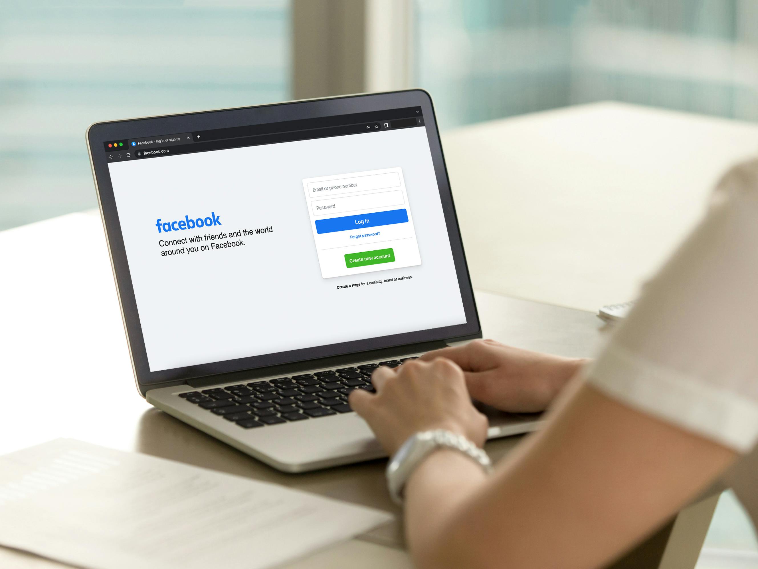 woman sitting at desk with laptop logging into facebook