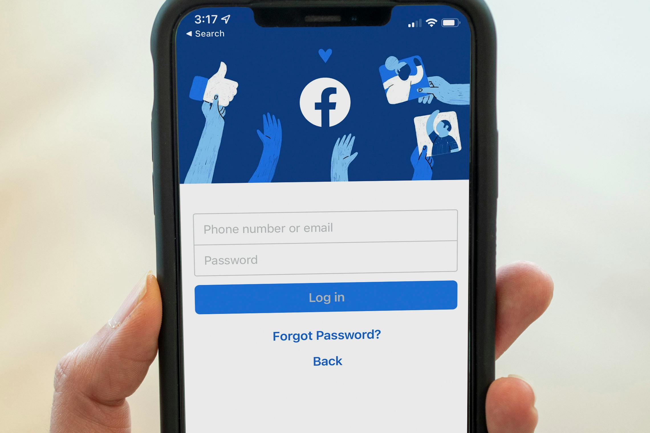 A close-up on an iPhone being held up, displaying the login page on the Facebook mobile app.