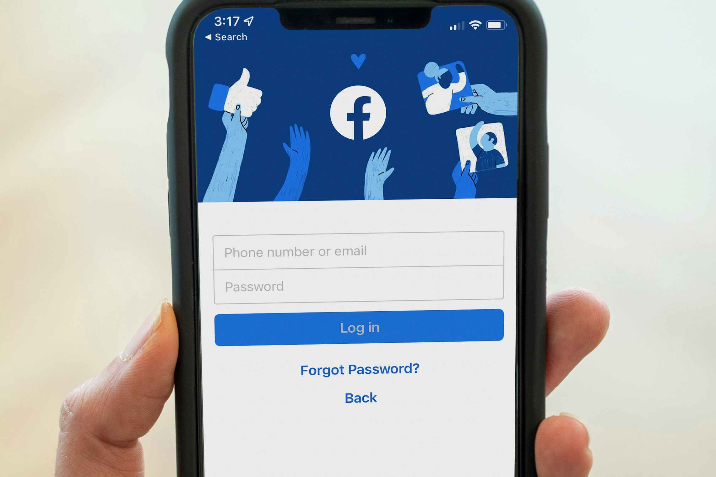 A close-up on an iPhone being held up, displaying the login page on the Facebook mobile app.