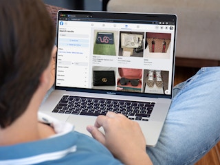 A person sitting on a couch, using a laptop that is displaying the Facebook Marketplace search results for Gucci.