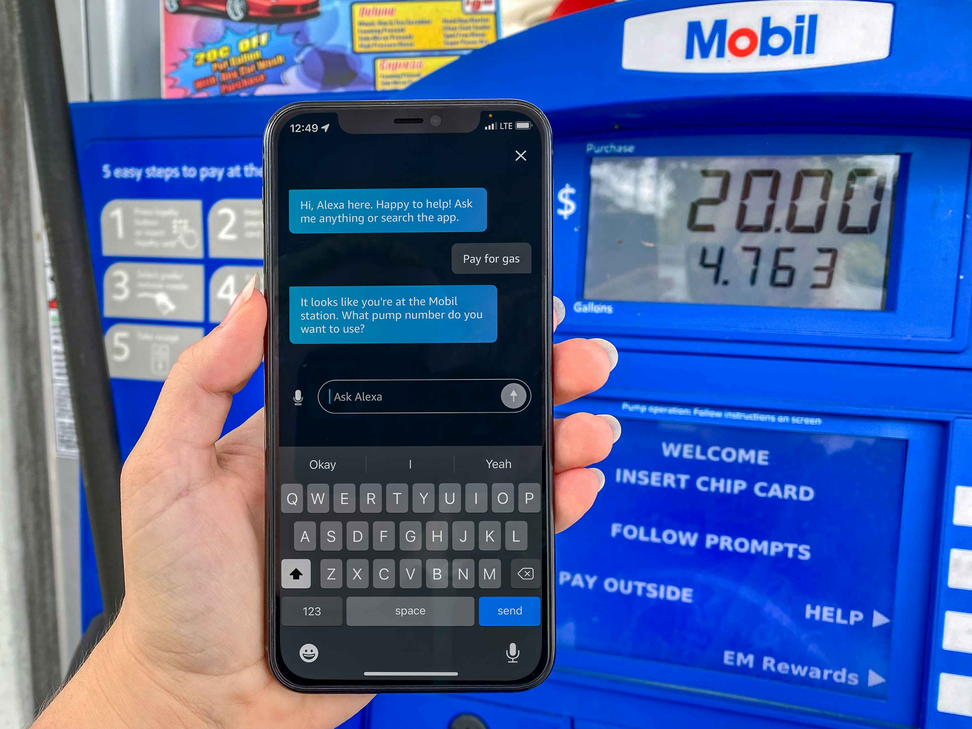 A person's hand holding up their iPhone, using the Amazon Alexa app to pay for gas at a Mobil gas station pump.
