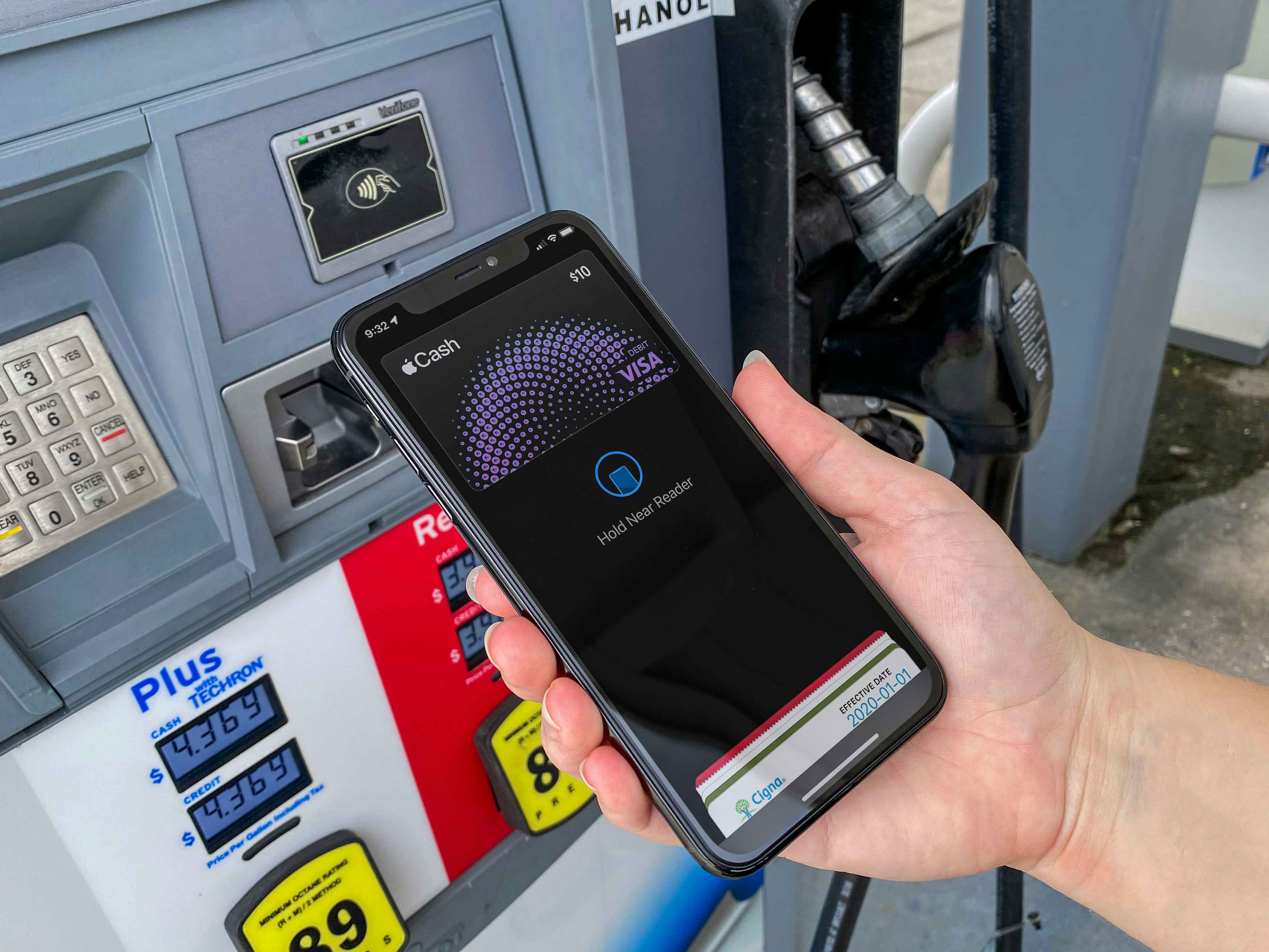 A person's hand holding their iPhone to the card reader on a gas pump with Apple Pay open on the screen.