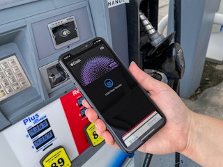 A person's hand holding their iPhone to the card reader on a gas pump with Apple Pay open on the screen.