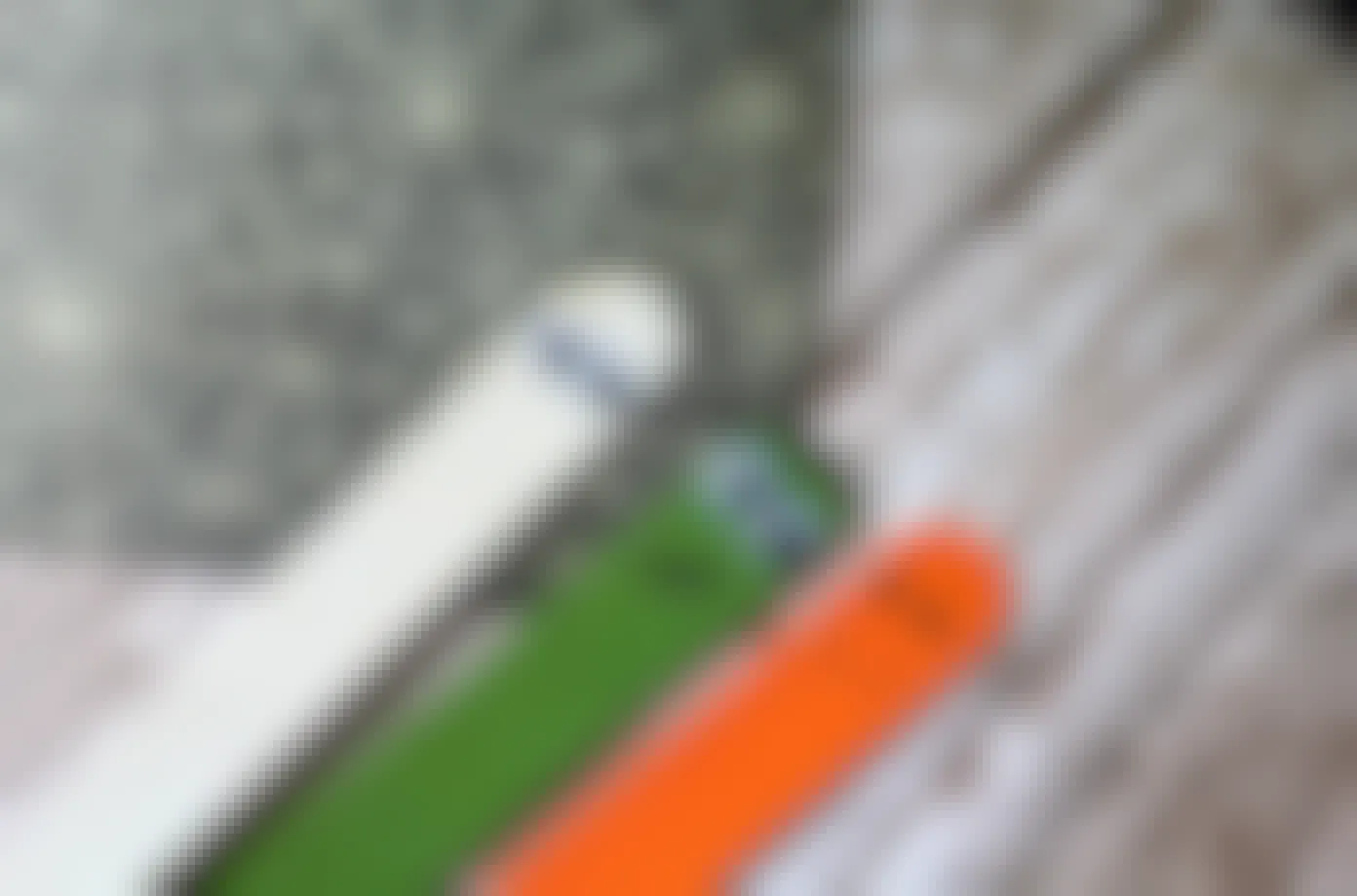 A white, green, and orange craft stick with googly eyes and a smiling face.