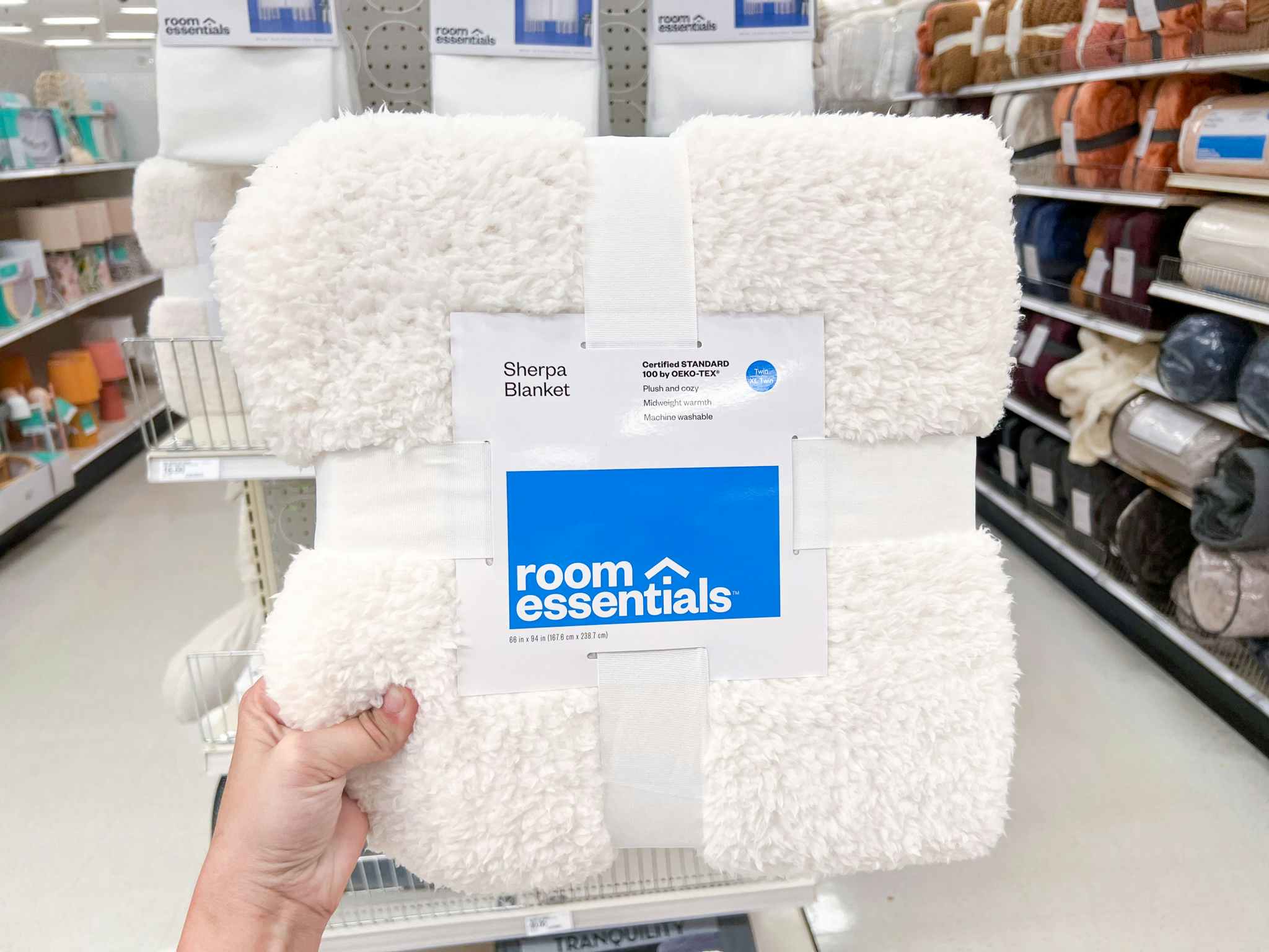 a hand holding a room essentials sherpa blanket in an aisle at target