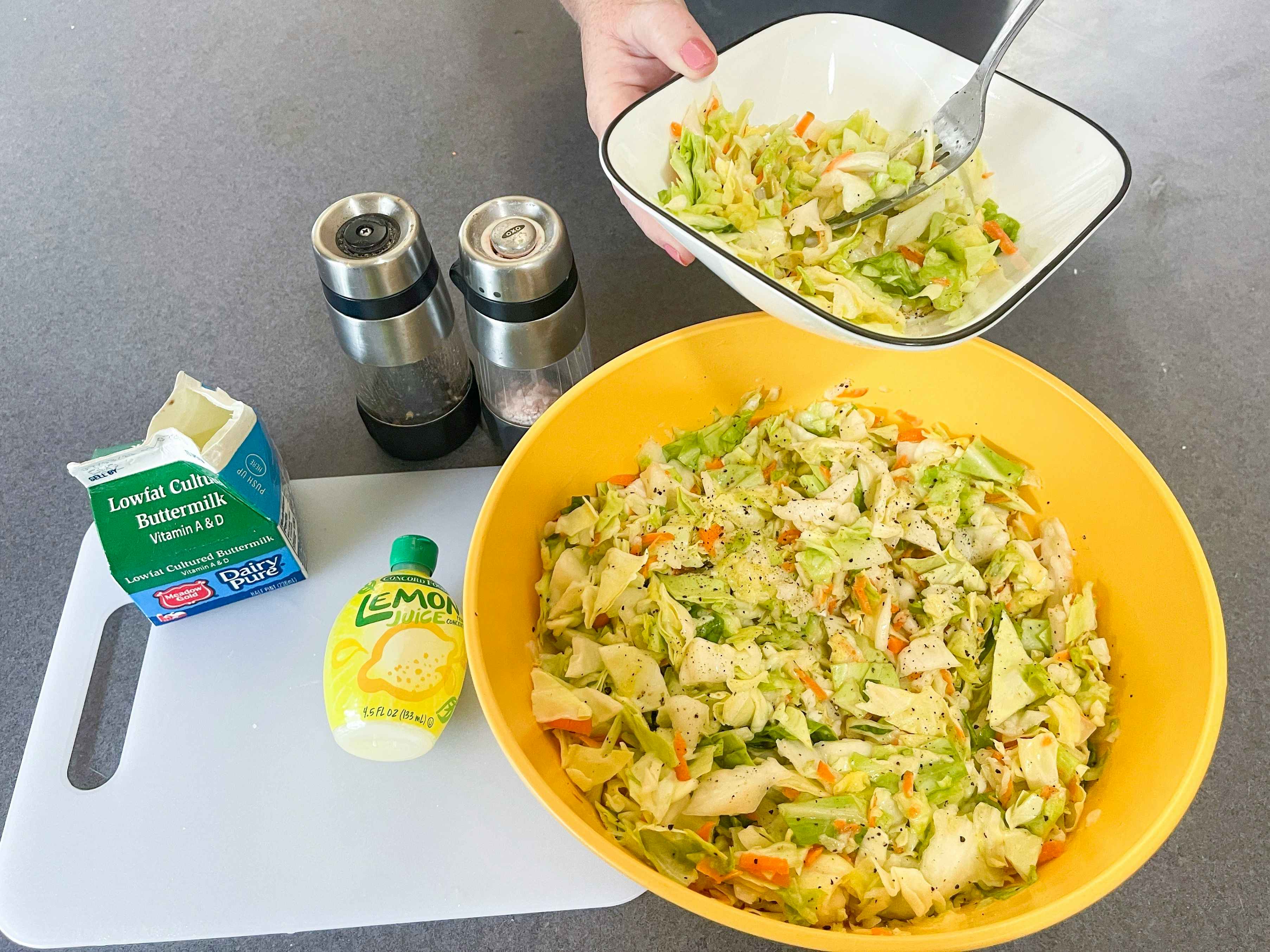 a person scooping diy homemade coleslaw from mixing bowl to smaller bowl to eat 